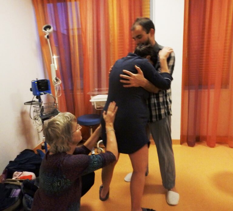 Malua geeft tegendruk op de rug terwijl de partner zijn vrouw vasthoudt tijdens de bevalling